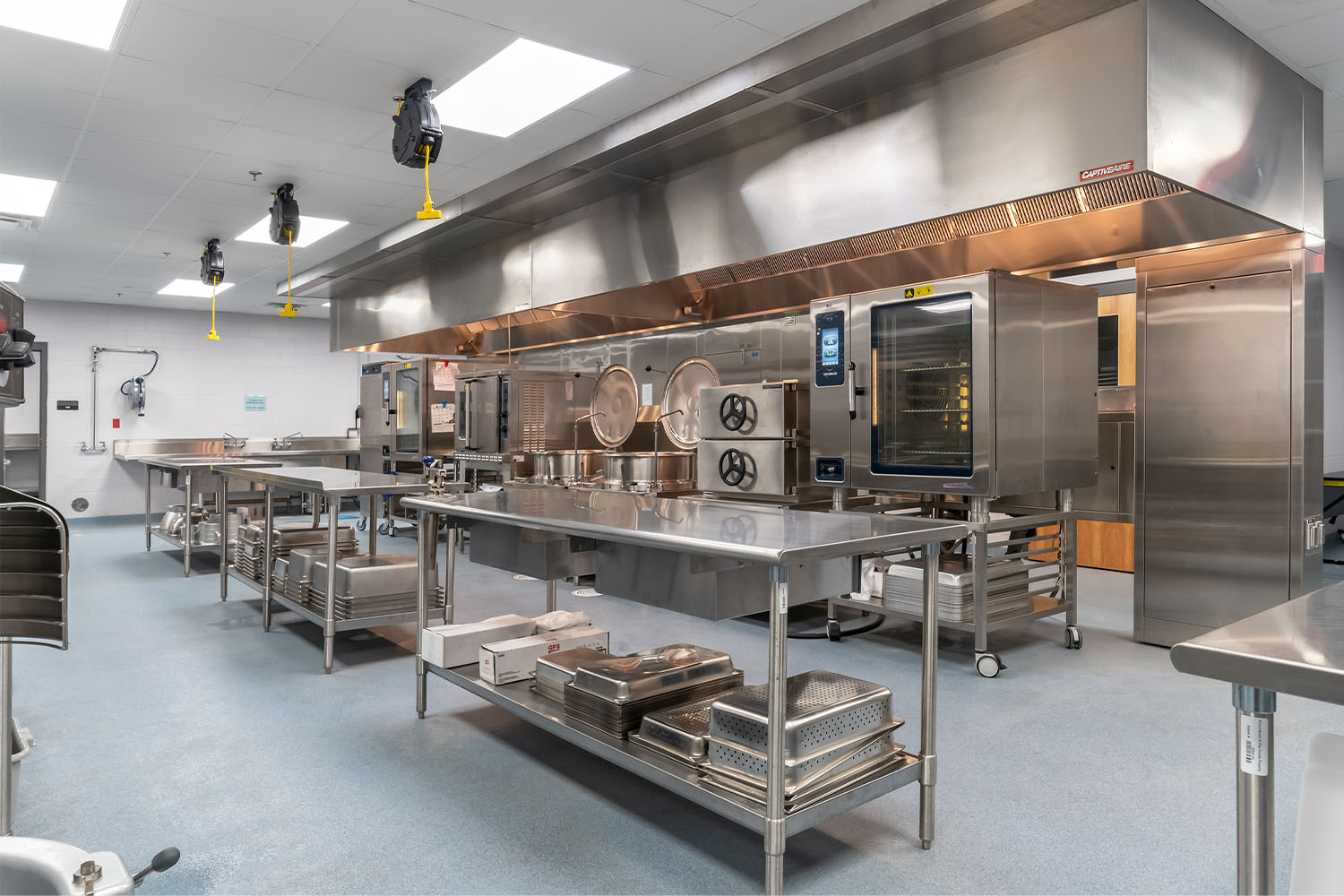 Kitchen with stainless steel equipment, food prep tables, ovens, exhaust hoods and serving trays