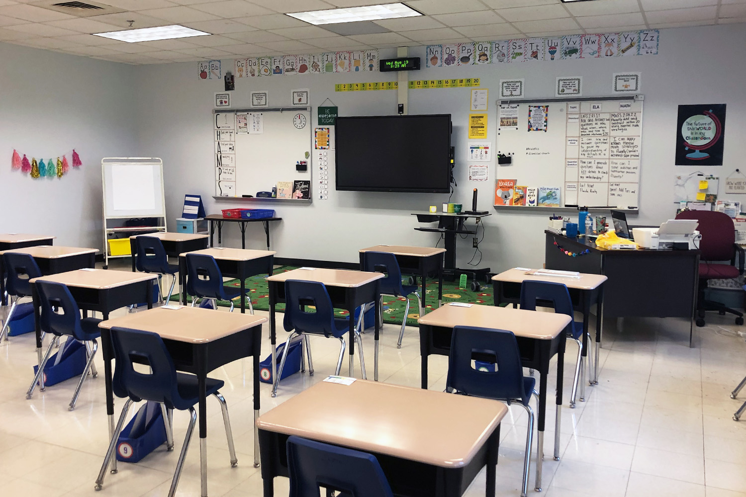 Elementary school classroom with desks, chairs, and wall-mounted T.V.